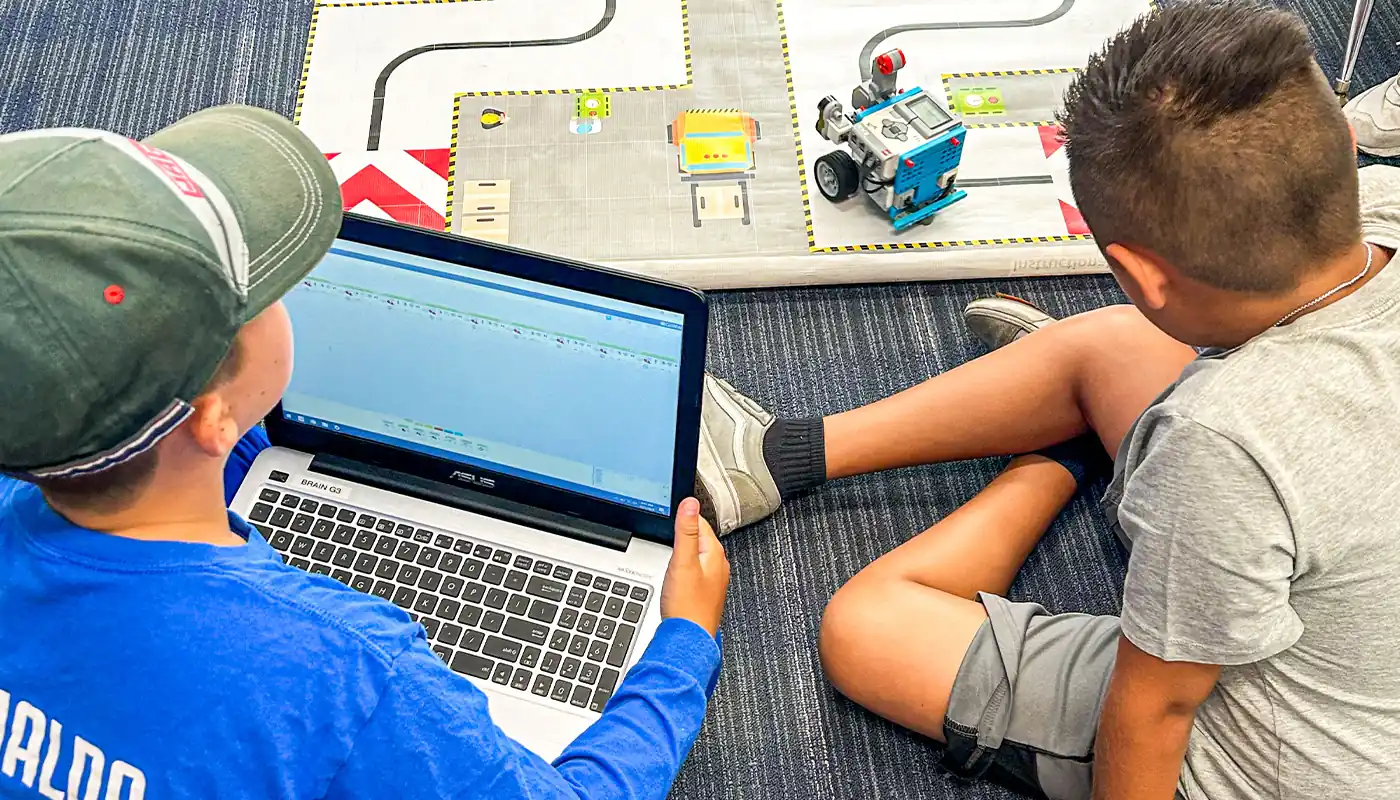 Students using a laptop and robotics equipment during a BrainStorm STEM lesson.