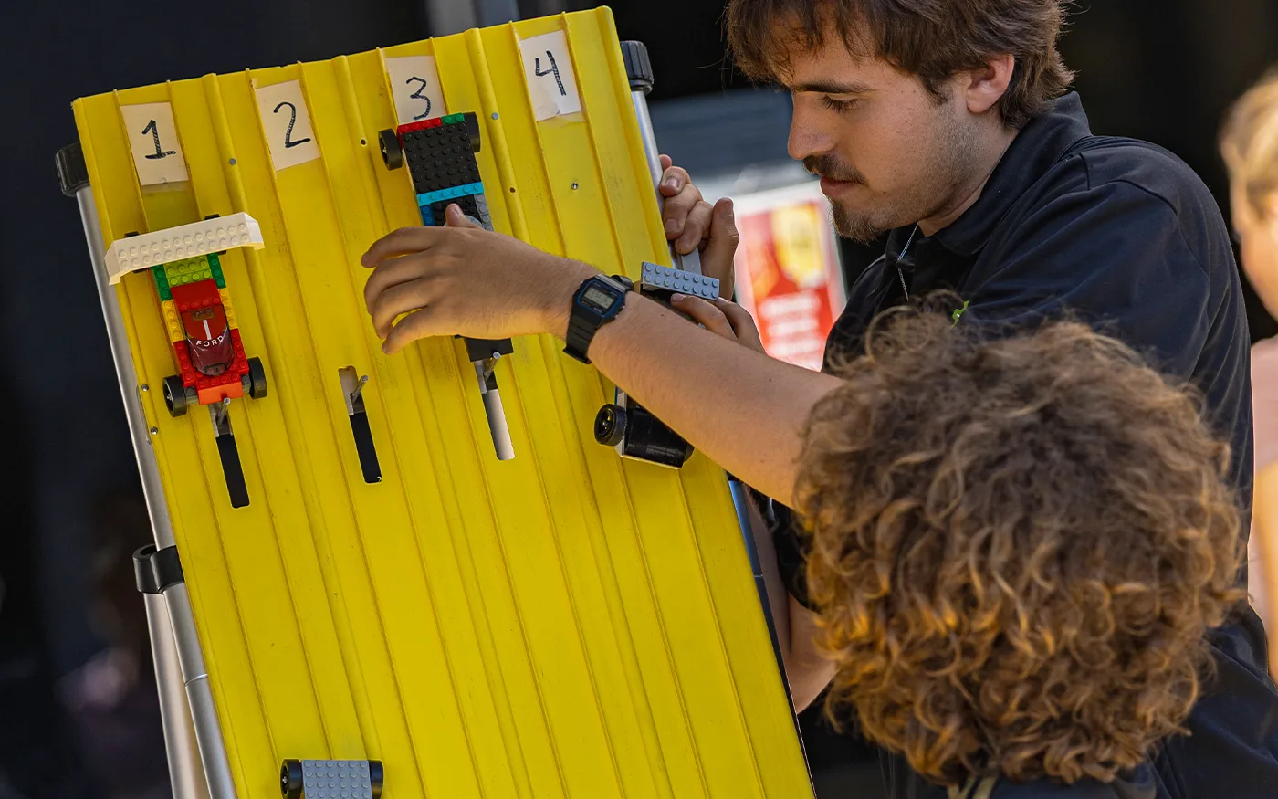 A BrainStorm instructor helping students prepare LEGO vehicles for a hands-on racing activity.