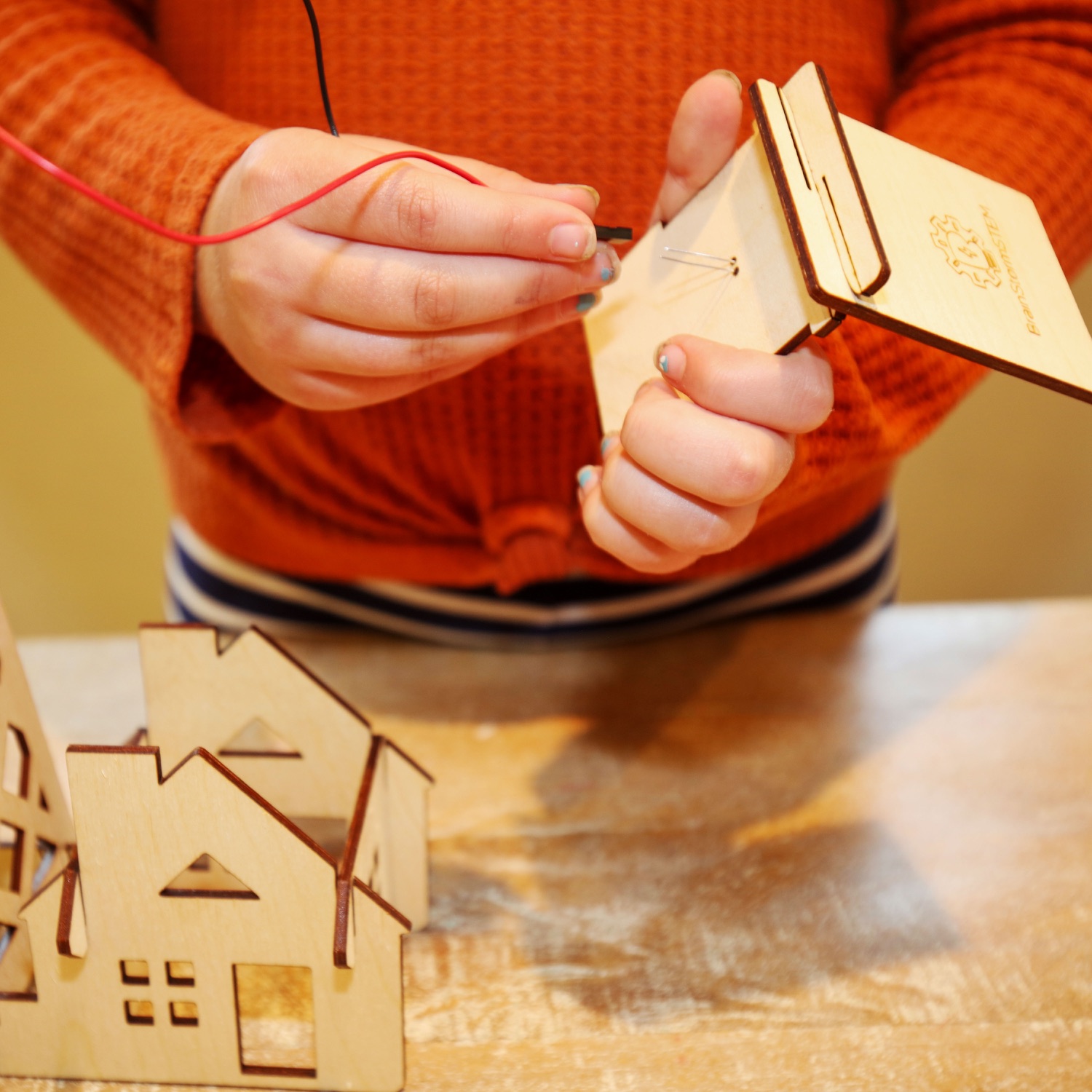 A student connects wires while assembling a wooden wind turbine model.