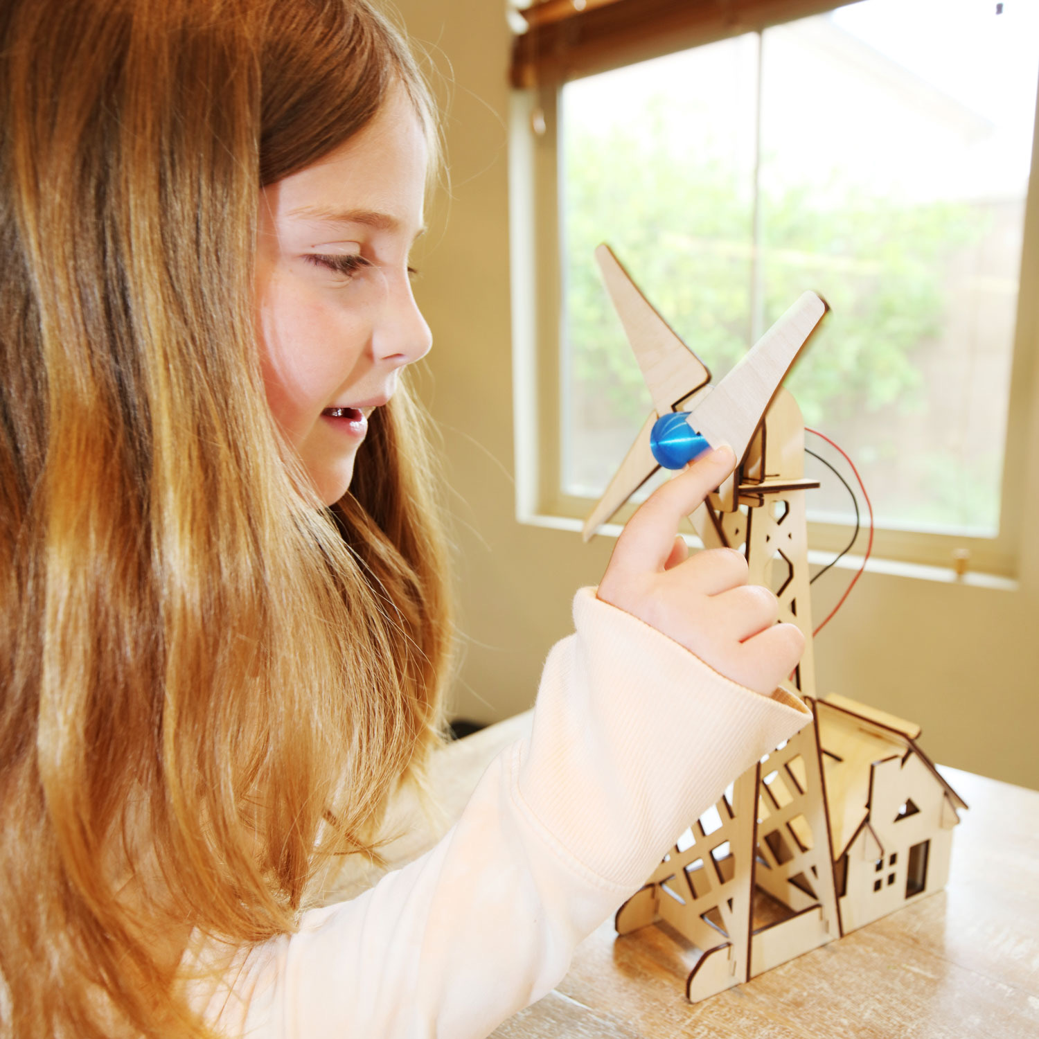 A student adjusts the blue hub on her wooden wind turbine model.
