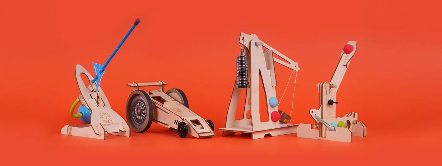Four BrainStorm STEM kits, a catapult, a solar racer, a trebuchet, and a ball-launching catapult, arranged together on a red background.